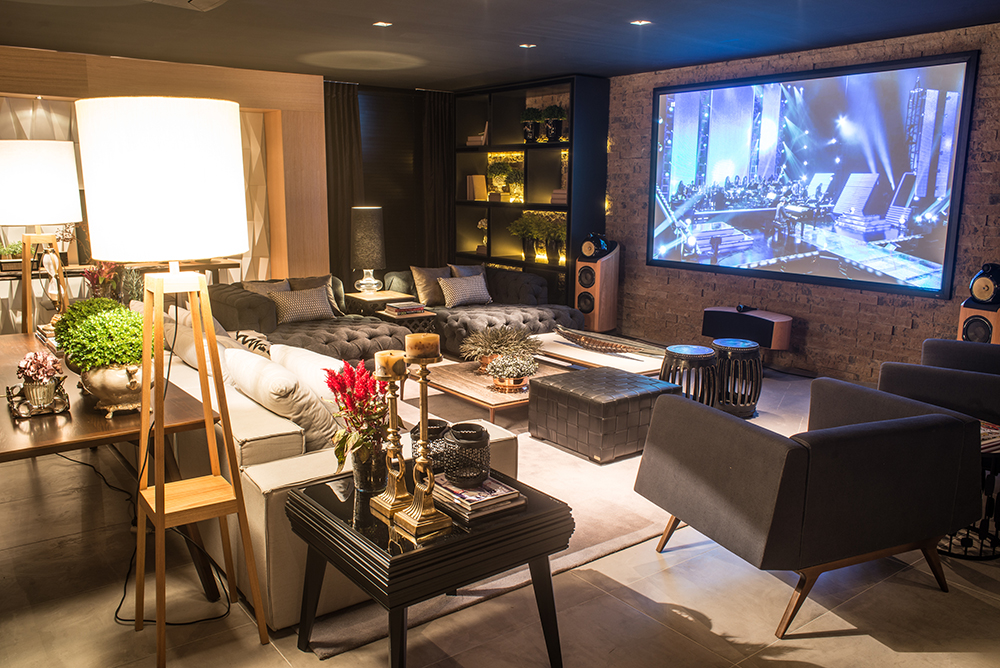 Home Theater - Aline Luccini. Poltronas e estofados generosos são um convite irresistível para a família receber amigos. Ao centro, mesinhas, pufe em couro e banquetas oferecem apoio e podem virar assentos extras. Móveis com estilo retrô e pés palito dialogam com a rusticidade das paredes em tijolos. Elas ainda conferem intimismo e fazem contraponto à alta tecnologia presente no ambiente de 105 m².