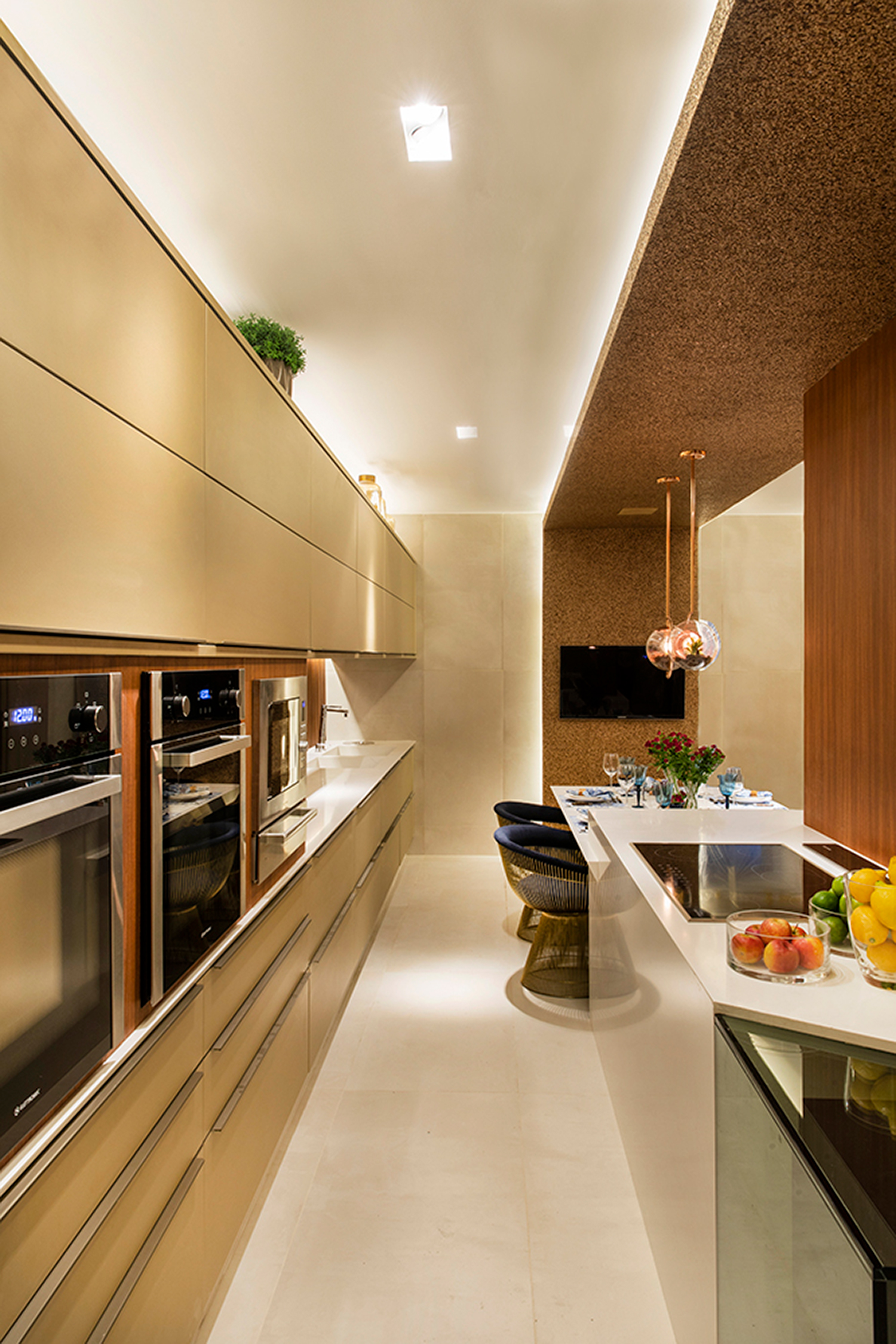 CASACOR Pernambuco. Cozinha Todeschini - Marylia Nogueira Arquitetura. Para transformar a cozinha em espaço de convívio, a ideia foi embutir os eletrodomésticos e adotar a linha minimalista no projeto. Os modulados aproveitam a extensão da área, com um visual que transmite profundidade e continuidade. A ilha central é demarcada pelo pórtico revestido em mica, tornando o ambiente uma extensão da área de receber.