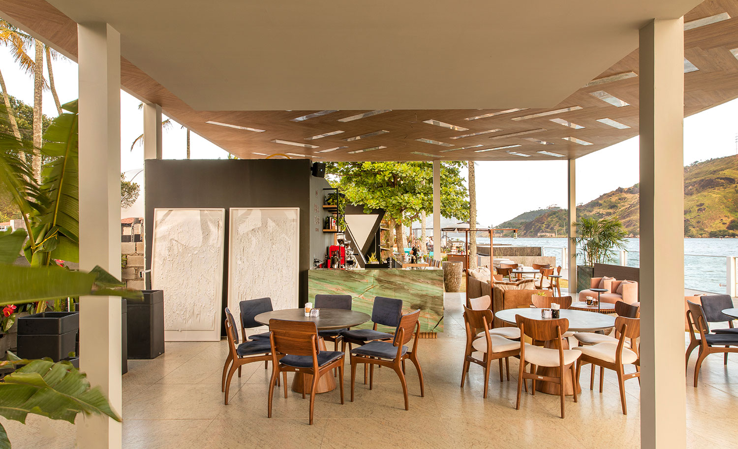 Coffee Work Apex - Amanda Leão, Bárbara Perim e Renata Morelato. O café é uma paixão brasileira, celebrado nestes 175 m². O espaço prioriza o conforto ambiental por meio da iluminação e da ventilação naturais, valorizando a bela vista do local e englobando a vegetação existente. Destaque especial para o teto, desenvolvido com réguas de madeira mescladas com ripas de pedras translúcidas, que atuam como luminárias.