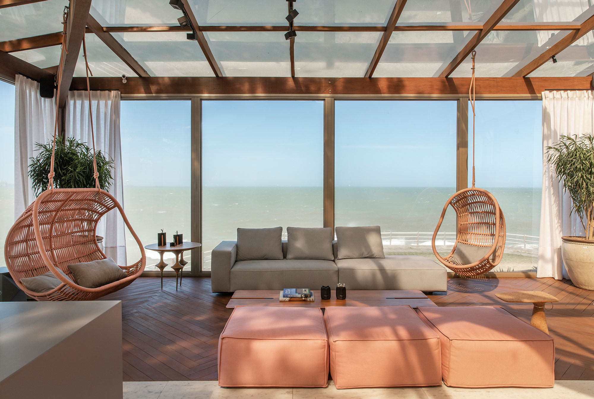 CASACOR Espírito Santo 2019. Lounge Sunset - Cyane Zoboli. A arquitetura se integra à paisagem e amplia o alcance da visão, sem perder o conforto de estar em casa. O ambiente de 130 m² emoldura a vista da baía de Vitória e aposta nos recursos naturais, como a madeira e o vidro que conferem simplicidade à estrutura. A ambientação projetada não veio ao acaso, destacando o uso de materiais rochosos, como granito e ardósia, e de madeiras para o deck e mobiliário.