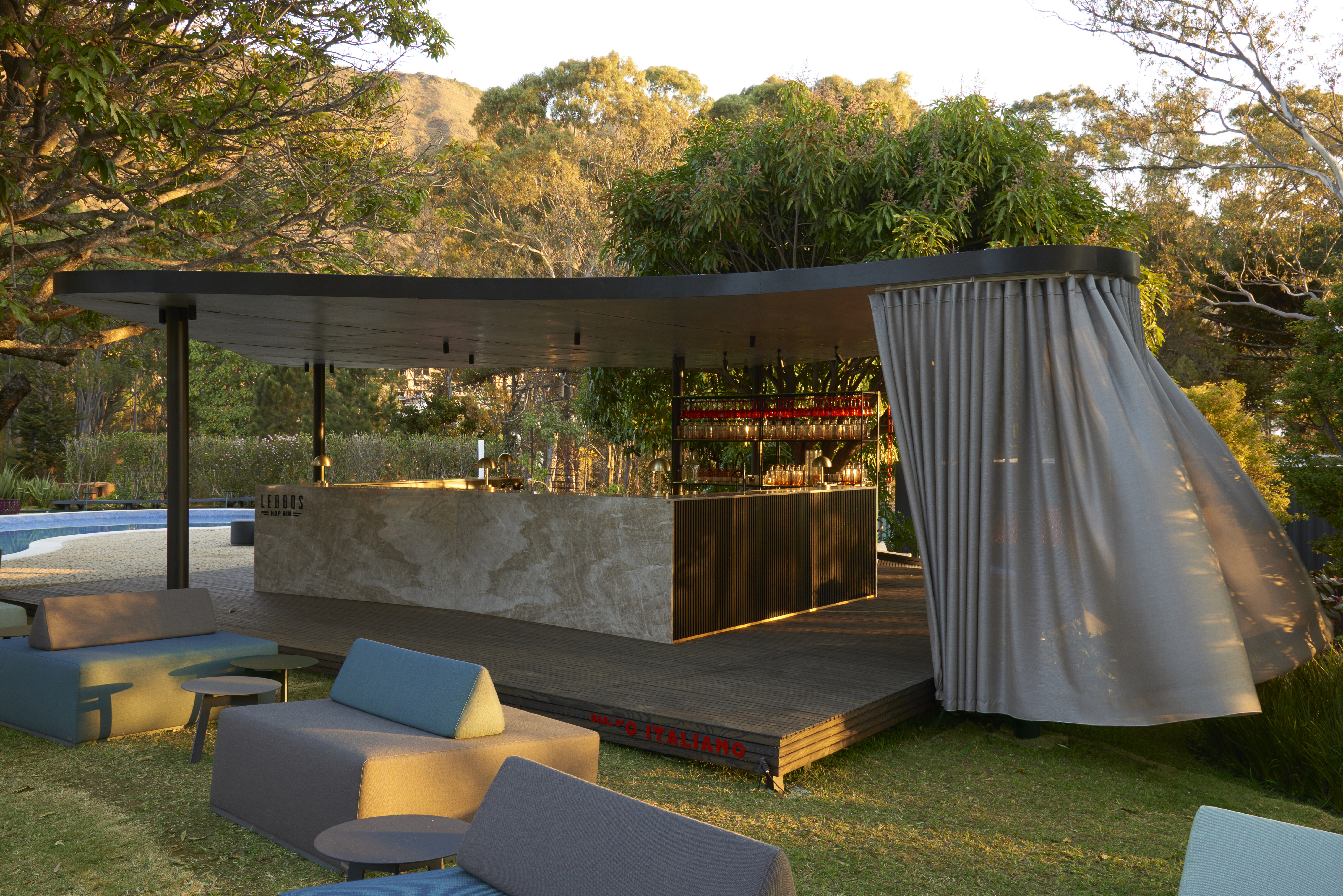 Bar - Lucas Lage. CASACOR Minas Gerais 2019. O bar de drinks foi inspirado nos rooftops novaiorquinos e sua forma orgânica se molda à piscina. O bar em madeira natural ganhou uma frente em pedra retroiluminada e, logo acima, as luminárias de latão escovado trazem pintura dourada em estilo art déco.