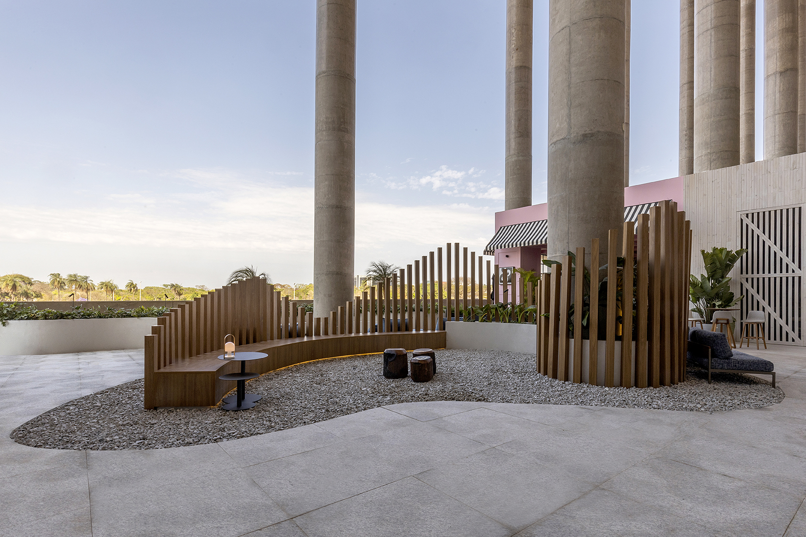 Studio Vírgula (Carolina Mesquita e Maria Paula Leite) - Praça Áurea. Tendo o horizonte da capital federal como pano de fundo, o ambiente de 400 m² foi criado pelo Studio Vírgula para proporcionar harmonia por meio do conceito do design biofílico. É um espaço de contemplação, onde os pilares redondos existentes no estádio conversam com as formas orgânicas do projeto. Destaque para os bancos criados para o ambiente que são envolvidos por jardins e a utilização de materiais naturais, como granito no piso e madeira no deck. Todo o mobiliário é assinado por designers brasileiros.