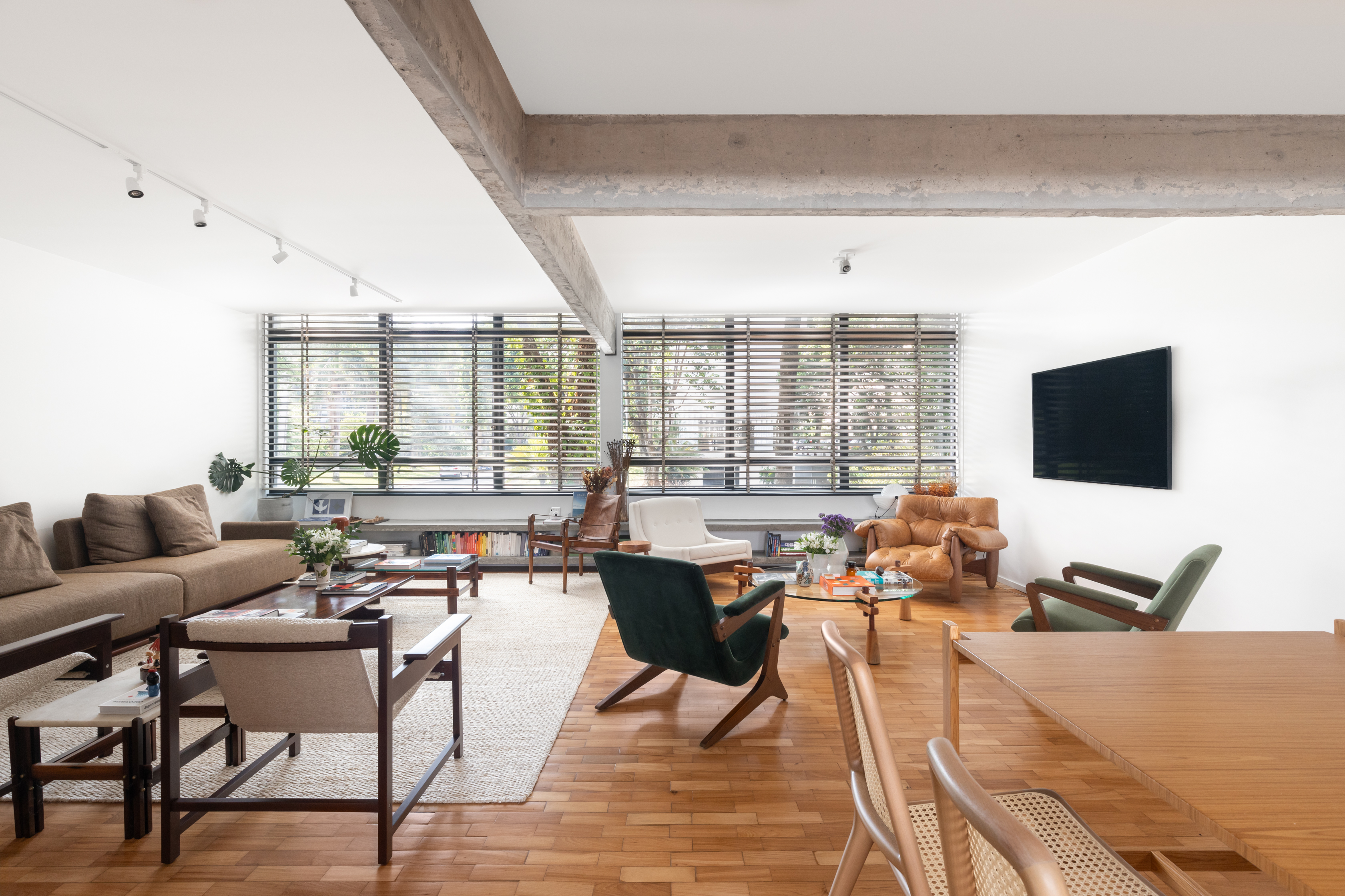 Reforma em apê de 150 m² valoriza a arquitetura modernista de Brasília. Projeto de Bloco Arquitetos. Na foto, sala de estar e jantar, com cortina, piso de madeira e poltrona.